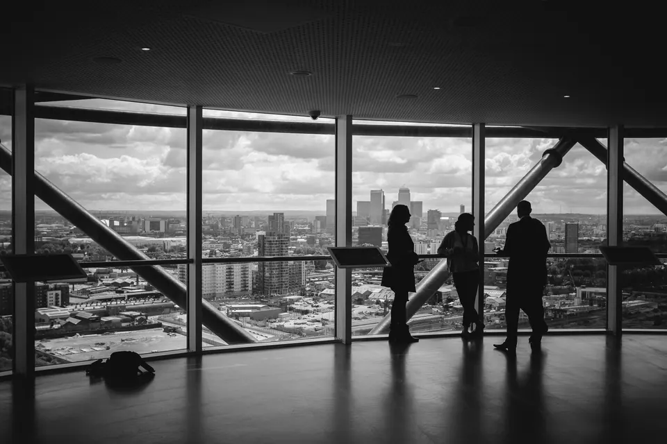 Three people in conversation beside large windows overlooking a city