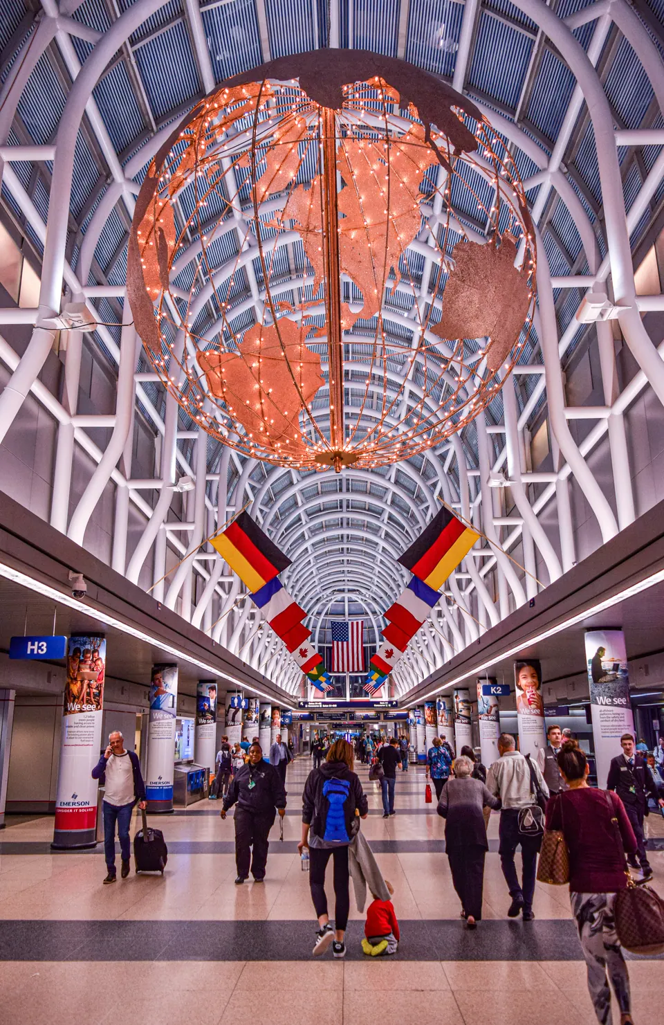 Travellers walking through an international airport beneath country flags and a globe installation